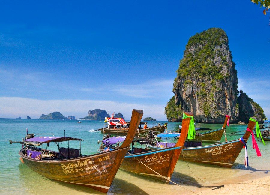 Longtail boats moored on a Thai beach below a limestone cliff